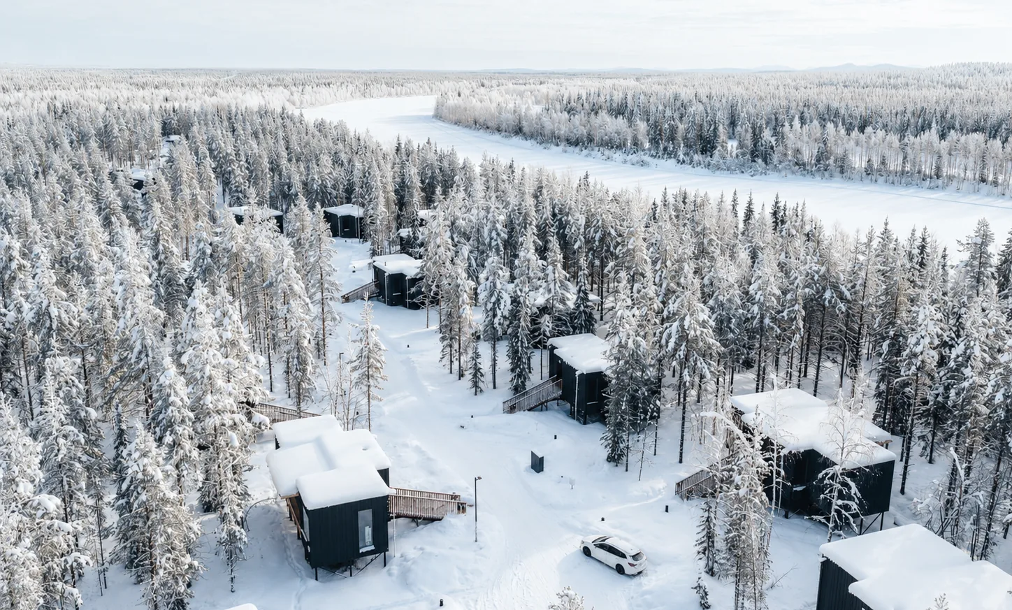 Aerial view of NOA Villas among snow-covered trees beside the river